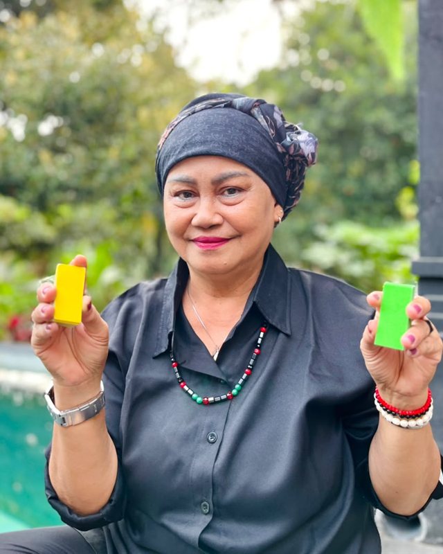 Mami Lisa smiling in a garden, holding up two small packs of cards